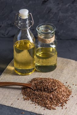 Bir yığın kaşık ve keten tohumu Keten tohumu altın cam şişe masanın üzerinde karanlık bir arka plan üzerinde yağda. Omega 3 yağ asitleri ile kavram sağlıklı beslenme.