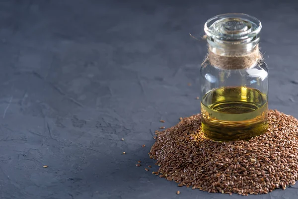 stock image Flax seeds in a pile and linseed golden oil in a glass bottle are on the table on a dark background. The concept healthy diet with omega 3 fatty acids.