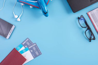 Uçak, uçak bileti, pasaport, gözlük ve telefon ile mavi bir arka plan üzerinde kulaklık. Üstten görünüm. Planlama ve seyahat için hazırlanıyor kavramı