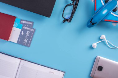 Uçak, uçak bileti, pasaport, dizüstü bilgisayar ve telefon ile mavi bir arka plan üzerinde kulaklık. Üstten görünüm. Planlama ve seyahat için hazırlanıyor kavramı
