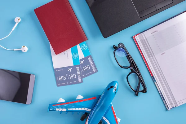 Plane, air tickets, passport, notebook and phone with headphones on a blue background. The view from the top. The concept of planning and preparing for the travel