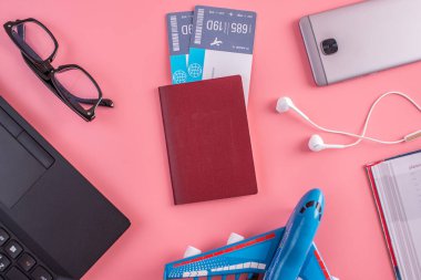 Uçak, uçak bileti, pasaport, dizüstü bilgisayar ve telefon kulaklık üzerinde pembe bir arka plan ile. Üstten görünüm. Planlama ve seyahat için hazırlanıyor kavramı