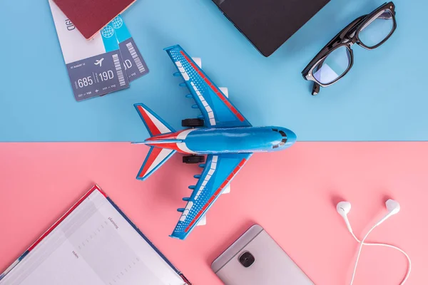 Plane, air tickets, passport, notebook and phone with headphones on pastel background. The view from the top. The concept of planning and preparing for the travel