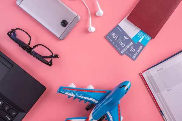 Plane, air tickets, passport, notebook and phone with headphones on a pink background. The view from the top. The concept of planning and preparing for the travel