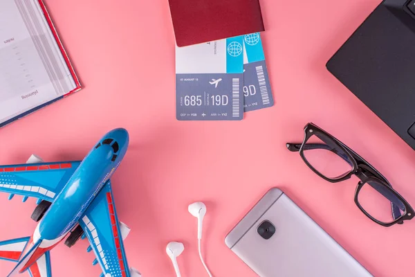 Plane, air tickets, passport, notebook and phone with headphones on a pink background. The view from the top. The concept of planning and preparing for the travel