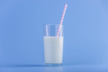 Bir bardak taze süt ile mavi bir arka plan üzerinde bir saman. Renkli minimalizm. Kalsiyum sağlıklı süt ürünleri kavramı