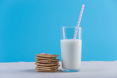 Bir bardak taze süt bir saman ve çerezler üzerinde mavi bir arka plan ile. Renkli minimalizm. Kalsiyum sağlıklı süt ürünleri kavramı