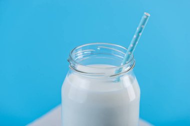 Cam şişe saman üzerinde mavi arka plan ile taze süt. Renkli minimalizm. Kalsiyum sağlıklı süt ürünleri kavramı