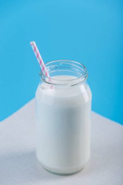 Cam şişe saman üzerinde mavi arka plan ile taze süt. Renkli minimalizm. Kalsiyum sağlıklı süt ürünleri kavramı
