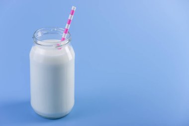 Cam şişe saman üzerinde mavi arka plan ile taze süt. Renkli minimalizm. Kalsiyum sağlıklı süt ürünleri kavramı