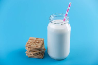 Cam şişe saman ve çerezler üzerinde mavi arka plan ile taze süt. Renkli minimalizm. Kalsiyum sağlıklı süt ürünleri kavramı
