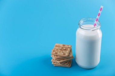 Cam şişe saman ve çerezler üzerinde mavi arka plan ile taze süt. Renkli minimalizm. Kalsiyum sağlıklı süt ürünleri kavramı