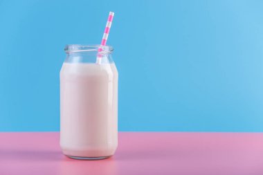 Cam şişe pastel arka plan üzerinde saman ile taze süt. Renkli minimalizm. Kalsiyum sağlıklı süt ürünleri kavramı