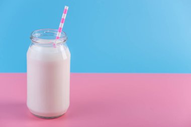 Cam şişe pastel arka plan üzerinde saman ile taze süt. Renkli minimalizm. Kalsiyum sağlıklı süt ürünleri kavramı