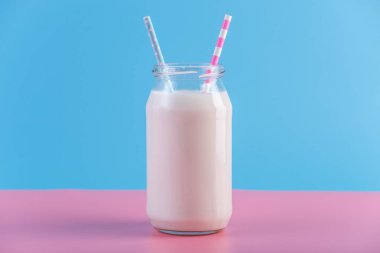 Cam şişe pastel arka plan üzerinde iki payet ile taze süt. Renkli minimalizm. Kalsiyum sağlıklı süt ürünleri kavramı