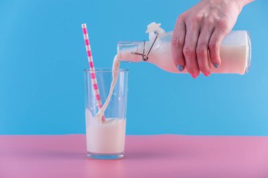 Bir kadın eli pastel bir arka plan üzerine bir bardak içine bir cam şişe taze süt dökülen. Renkli minimalizm. Kalsiyum sağlıklı süt ürünleri kavramı