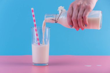 Bir kadın eli pastel bir arka plan üzerine bir bardak içine bir cam şişe taze süt dökülen. Renkli minimalizm. Kalsiyum sağlıklı süt ürünleri kavramı