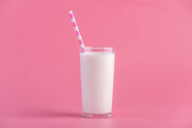 Bir bardak taze süt pembe bir arka plan üzerinde bir saman ile. Renkli minimalizm. Kalsiyum sağlıklı süt ürünleri kavramı