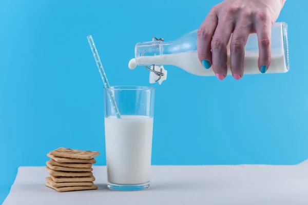 女性の手は ガラスと青い背景上の Cookie にガラス瓶から新鮮な牛乳を注ぐ カラフルなミニマリズム カルシウムと健康的な乳製品の概念 — ストック写真