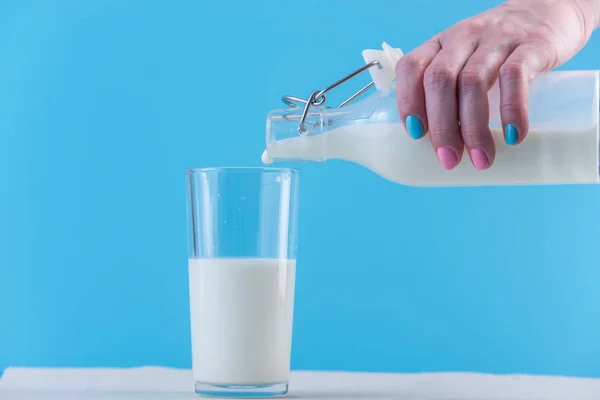 Woman Hand Pours Fresh Milk Glass Bottle Glass Blue Background — Stock Photo, Image