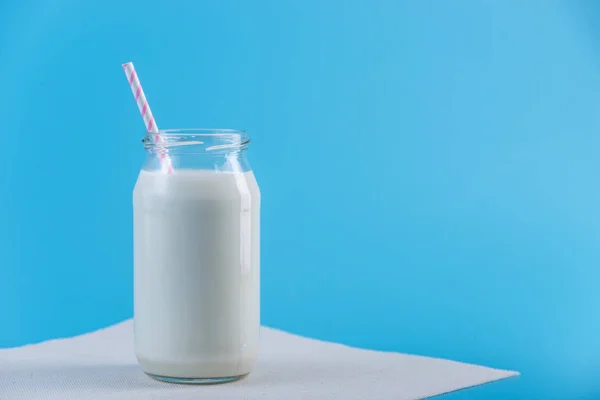 藁の上に青色の背景色と新鮮な牛乳のガラス瓶 カラフルなミニマリズム カルシウムと健康的な乳製品の概念 — ストック写真
