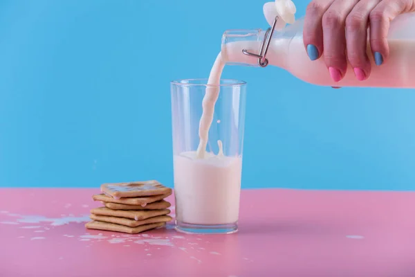 여자의 유리와 파스텔 배경에 쿠키에 병에서 신선한 우유를 따른다 다채로운 — 스톡 사진