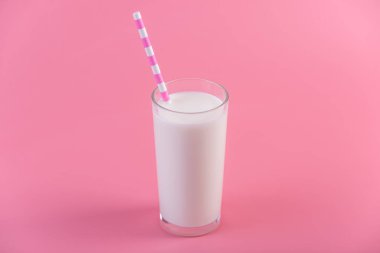 Bir bardak taze süt pembe bir arka plan üzerinde bir saman ile. Renkli minimalizm. Kalsiyum sağlıklı süt ürünleri kavramı