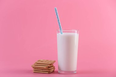 Bir bardak taze süt bir saman ve çerezler üzerinde pembe bir arka plan ile. Renkli minimalizm. Kalsiyum sağlıklı süt ürünleri kavramı