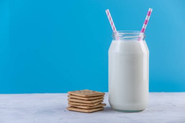 Cam şişe saman ve çerezler üzerinde mavi arka plan ile taze süt. Renkli minimalizm. Kalsiyum sağlıklı süt ürünleri kavramı