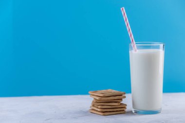 Bir bardak taze süt bir saman ve çerezler üzerinde mavi bir arka plan ile. Renkli minimalizm. Kalsiyum sağlıklı süt ürünleri kavramı