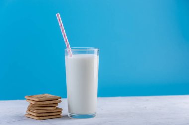 Bir bardak taze süt bir saman ve çerezler üzerinde mavi bir arka plan ile. Renkli minimalizm. Kalsiyum sağlıklı süt ürünleri kavramı