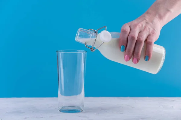 Woman Hand Pours Fresh Milk Glass Bottle Glass Blue Background — Stock Photo, Image