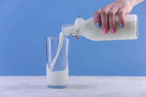 Woman Hand Pours Fresh Milk Glass Bottle Glass Blue Background — Stock Photo, Image