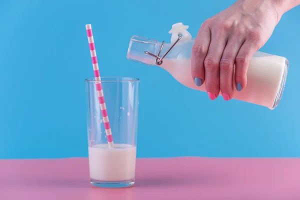 一个女人的手把新鲜的牛奶从玻璃瓶倒入一个柔和的背景玻璃 多彩简约 健康乳制品与钙的概念 — 图库照片
