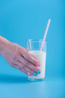 Bir kadın eli bir bardak taze süt bir saman ile mavi bir arka plan üzerinde tutar. Renkli minimalizm. Kalsiyum sağlıklı süt ürünleri kavramı