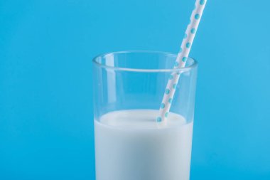 Bir bardak taze süt ile mavi bir arka plan üzerinde bir saman. Renkli minimalizm. Kalsiyum sağlıklı süt ürünleri kavramı