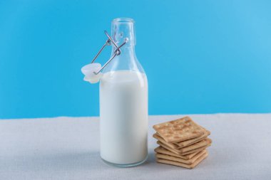 Taze süt ve kurabiye mavi arka plan üzerinde bir cam şişe. Renkli minimalizm. Kalsiyum sağlıklı süt ürünleri kavramı