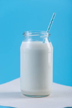 Cam şişe saman üzerinde mavi arka plan ile taze süt. Renkli minimalizm. Kalsiyum sağlıklı süt ürünleri kavramı