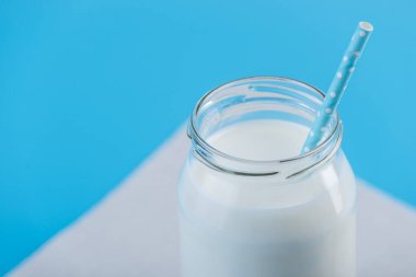 Cam şişe saman üzerinde mavi arka plan ile taze süt. Renkli minimalizm. Kalsiyum sağlıklı süt ürünleri kavramı