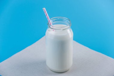 Cam şişe saman üzerinde mavi arka plan ile taze süt. Renkli minimalizm. Kalsiyum sağlıklı süt ürünleri kavramı