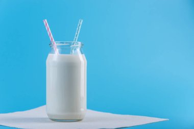 Cam şişe mavi zemin üzerine iki payet ile taze süt. Renkli minimalizm. Kalsiyum sağlıklı süt ürünleri kavramı