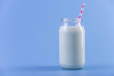 Cam şişe saman üzerinde mavi arka plan ile taze süt. Renkli minimalizm. Kalsiyum sağlıklı süt ürünleri kavramı