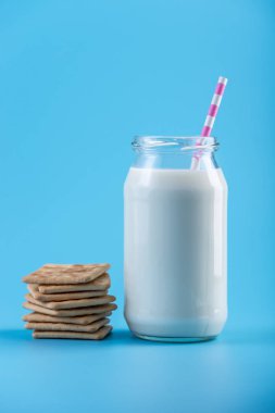 Cam şişe saman ve çerezler üzerinde mavi arka plan ile taze süt. Renkli minimalizm. Kalsiyum sağlıklı süt ürünleri kavramı