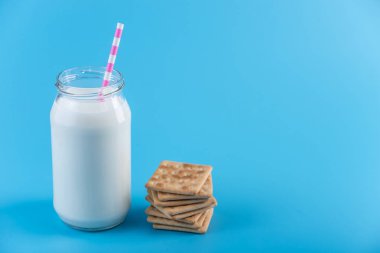 Cam şişe saman ve çerezler üzerinde mavi arka plan ile taze süt. Renkli minimalizm. Kalsiyum sağlıklı süt ürünleri kavramı