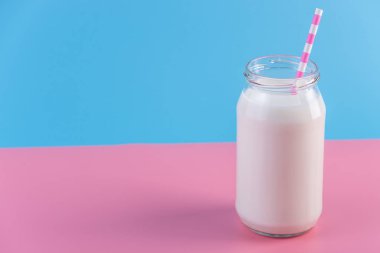 Cam şişe pastel arka plan üzerinde saman ile taze süt. Renkli minimalizm. Kalsiyum sağlıklı süt ürünleri kavramı