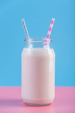 Cam şişe pastel arka plan üzerinde iki payet ile taze süt. Renkli minimalizm. Kalsiyum sağlıklı süt ürünleri kavramı