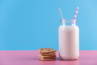 Cam şişe iki saman ve pastel arka plan üzerinde çerezler ile taze süt. Renkli minimalizm. Kalsiyum sağlıklı süt ürünleri kavramı
