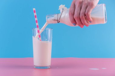 Bir kadın eli pastel bir arka plan üzerine bir bardak içine bir cam şişe taze süt dökülen. Renkli minimalizm. Kalsiyum sağlıklı süt ürünleri kavramı