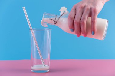 Bir kadın eli pastel bir arka plan üzerine bir bardak içine bir cam şişe taze süt dökülen. Renkli minimalizm. Kalsiyum sağlıklı süt ürünleri kavramı