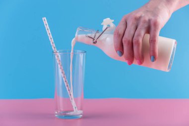 Bir kadın eli pastel bir arka plan üzerine bir bardak içine bir cam şişe taze süt dökülen. Renkli minimalizm. Kalsiyum sağlıklı süt ürünleri kavramı